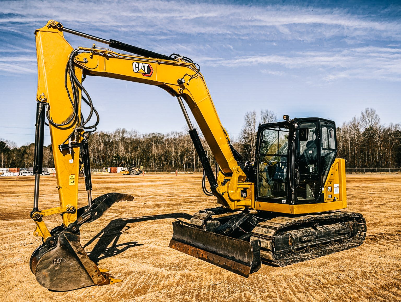 Malé pásové rýpadlo Caterpillar 308 s lyžicou v areáli so zemitým podkladom