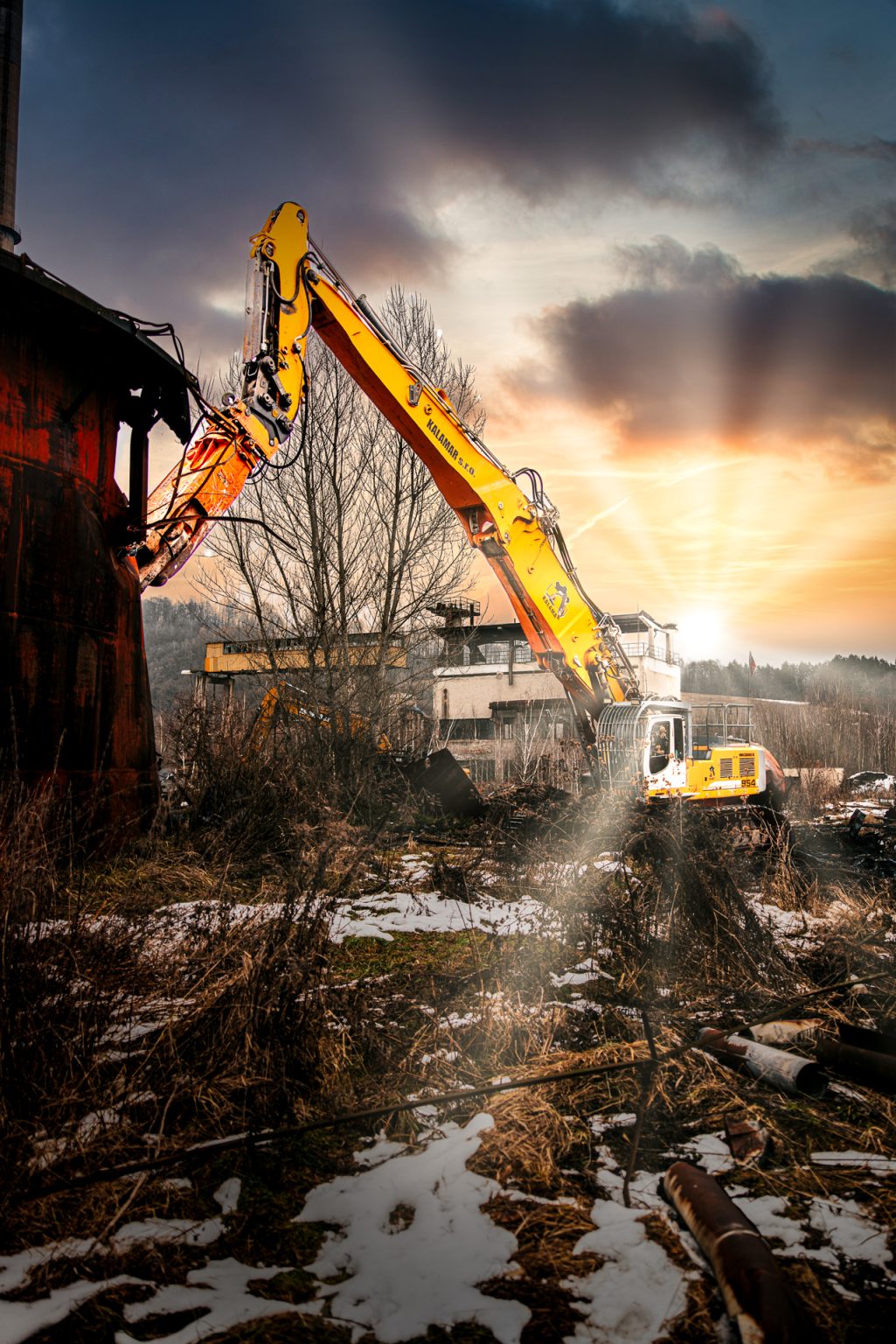 Pásové rýpadlo Liebherr R 954 C spoločnosti Kalamár s.r.o. so zdvihnutým dlhým ramenom a búracou nožnicou v priemyselnom areáli pri demolovaní kovovej nádrže na ropu. Demolačné práce.