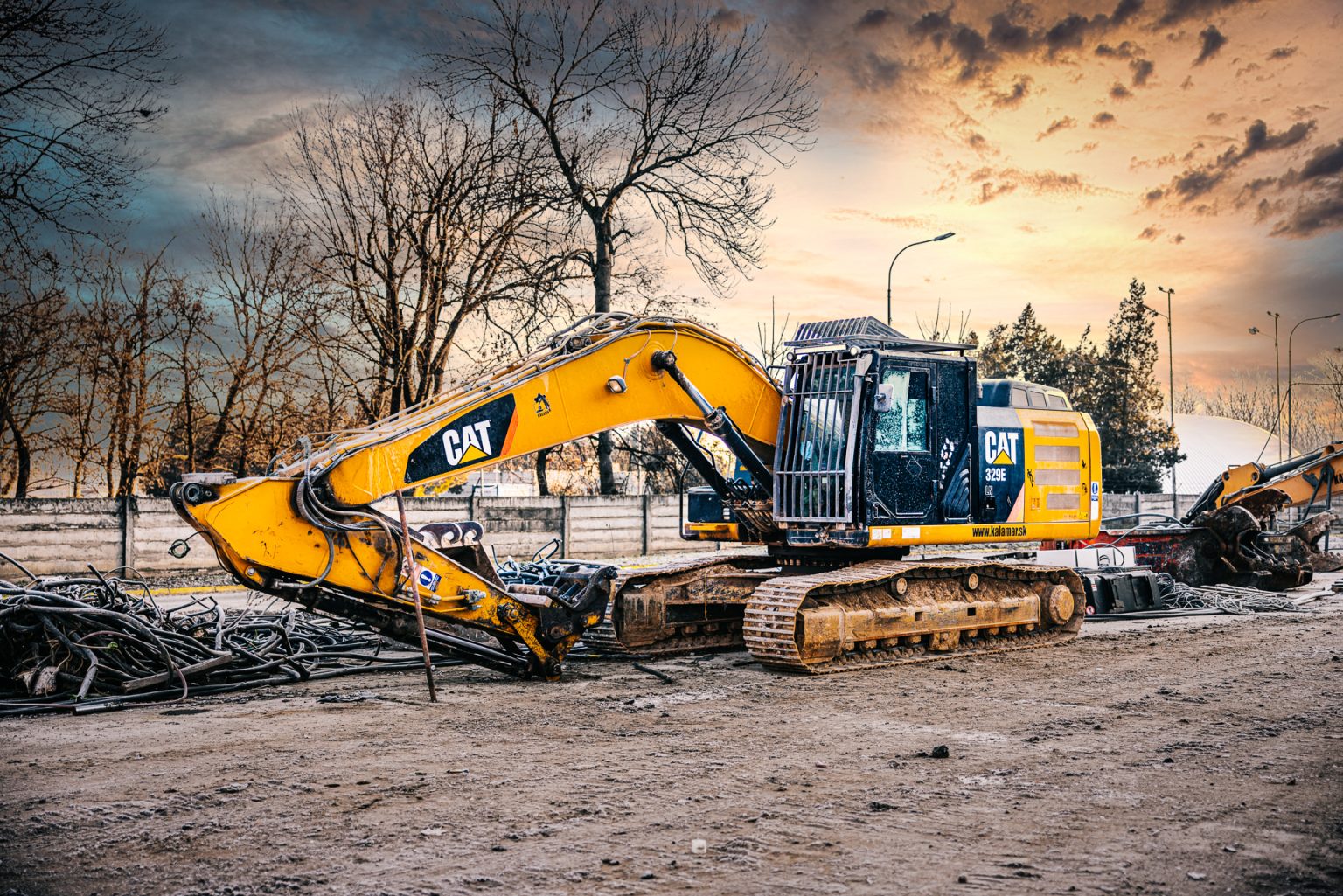 Pásové rýpadlo Caterpillar 329E na odstavnom parkovisku v priemyselnej zóne počas demolačných prác