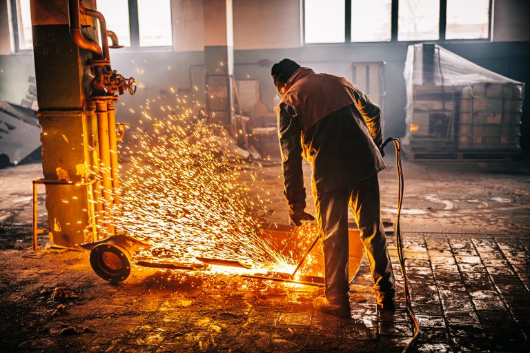 Palič s plazmovým horákom rozpaľuje časť kovovej nádrže v budove v priemyselnom areáli.