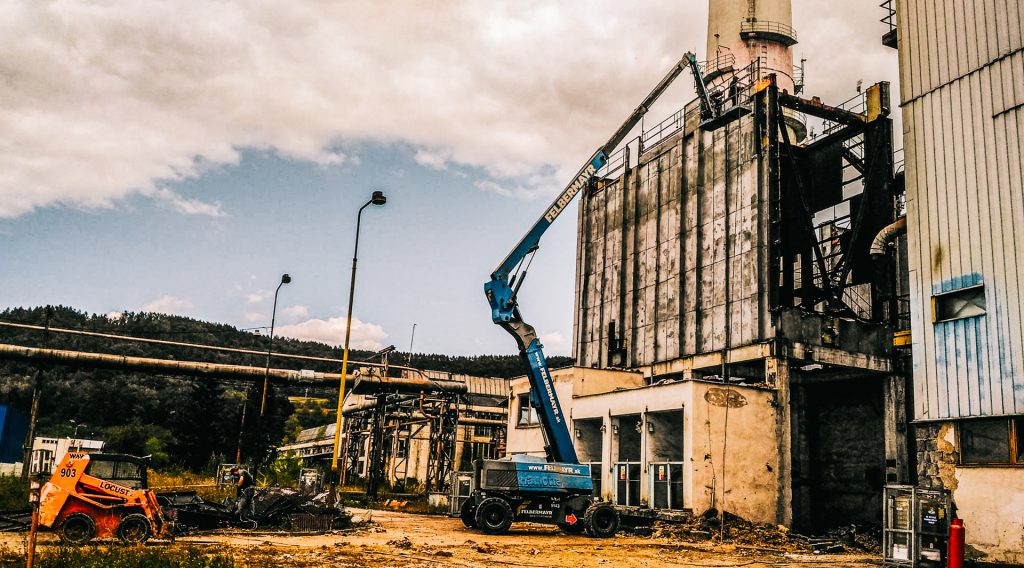 Vysokozdvižná plošina s vysunutým ramenom pri demolácii priemysleného objektu